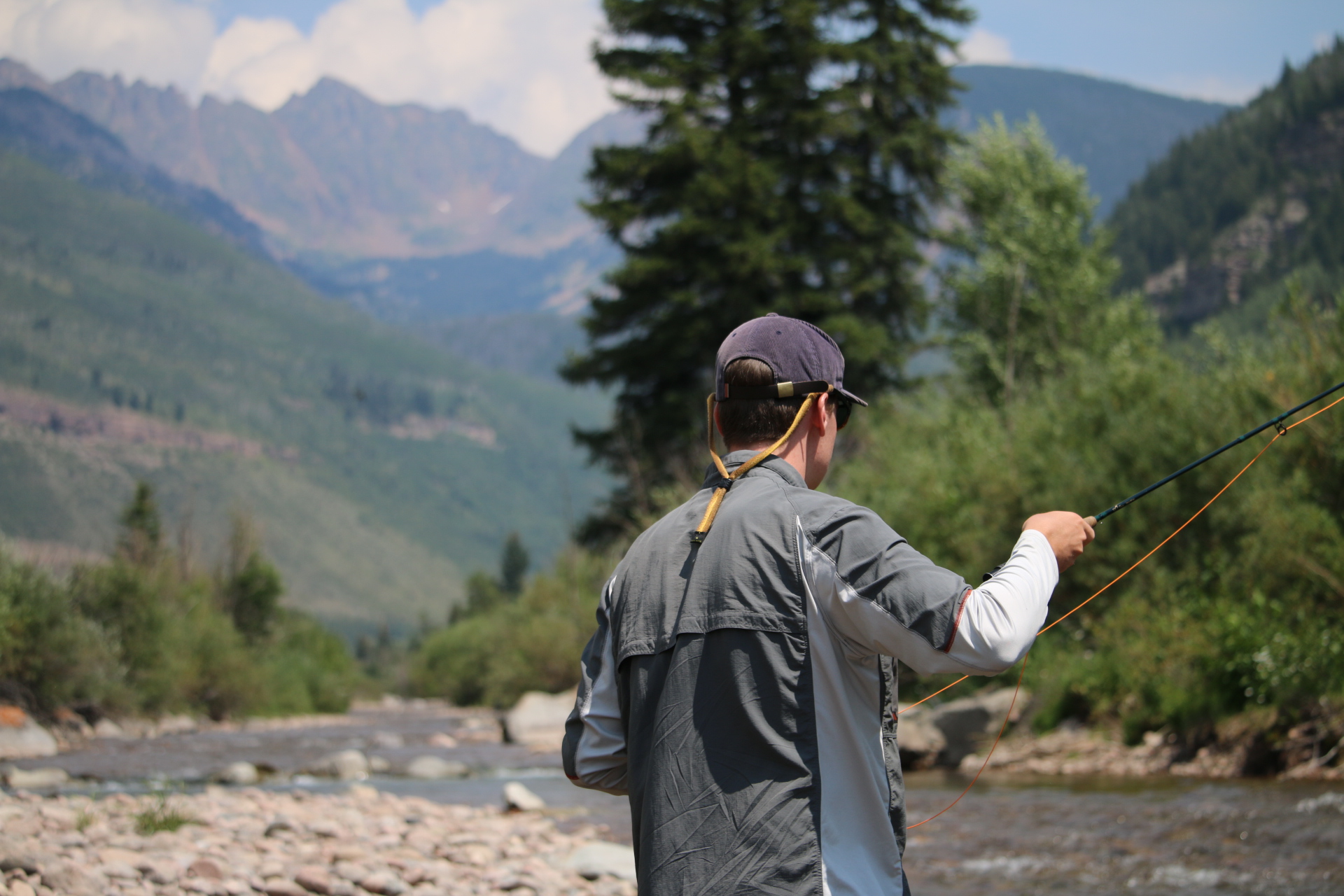 Person casting on Gore Creek with mountains in the background.